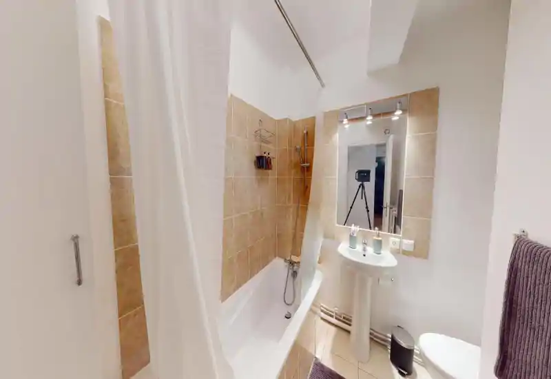 Clean, well-lit bathroom with a bathtub and shower, pedestal sink, illuminated mirror and modern fixtures.