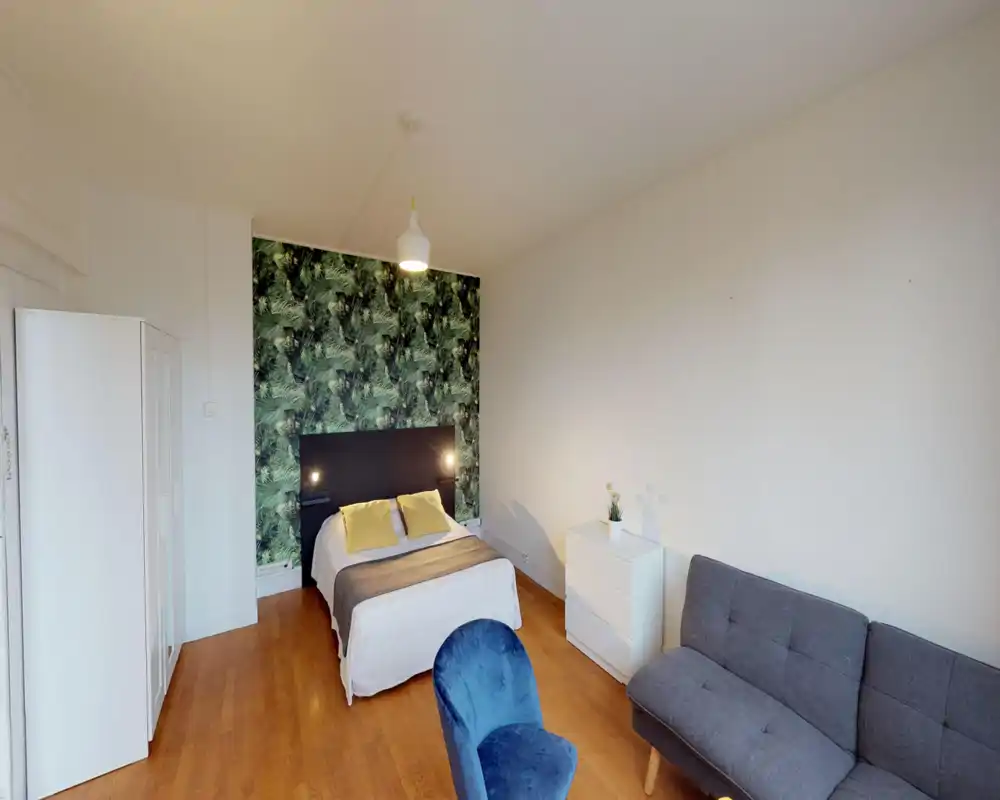 Camera da letto luminosa e ben allestita con letto matrimoniale davanti a una parete decorativa a foglie, lampade da comodino, armadio bianco e cassettiera. Stile confortevole con pavimento in legno.