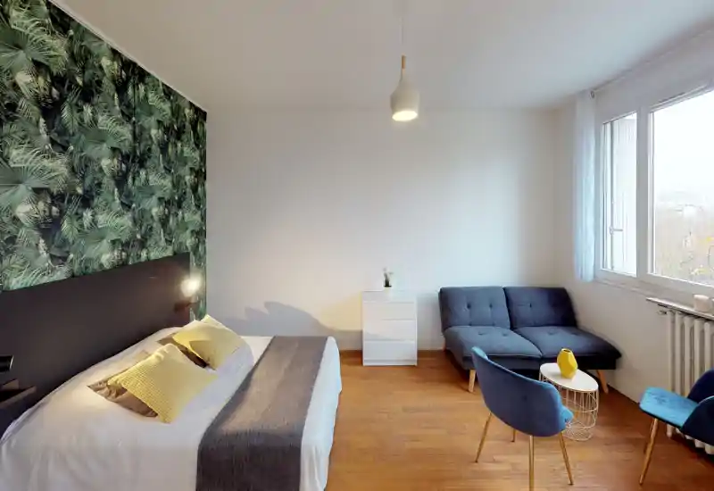 Camera da letto luminosa e moderna con letto matrimoniale confortevole, cuscini decorativi e una parete d'accento con motivo fogliame. Un angolo salotto vicino alla finestra offre spazio per rilassarsi.