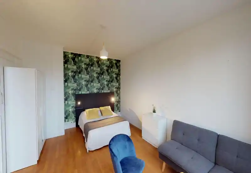Camera da letto luminosa e ben allestita con letto matrimoniale davanti a una parete decorativa a foglie, lampade da comodino, armadio bianco e cassettiera. Stile confortevole con pavimento in legno.