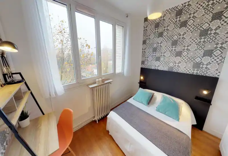 Chambre lumineuse et soignée avec un mur à motifs, grande fenêtre et lit double bien fait avec coussins turquoise — idéale pour une annonce.