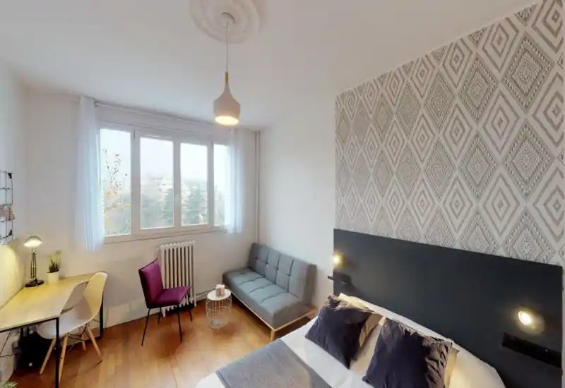 Chambre lumineuse et soignée avec lit double, mur d'accent à motif géométrique, petit canapé et bureau près de la fenêtre — parfaite pour un séjour confortable et lumineux.