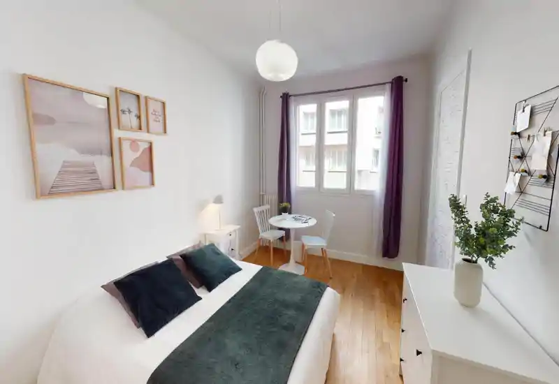 Bright bedroom with a double bed, light walls and a small plant; the photo is heavily distorted by digital artifacts but shows a cosy sleeping area.