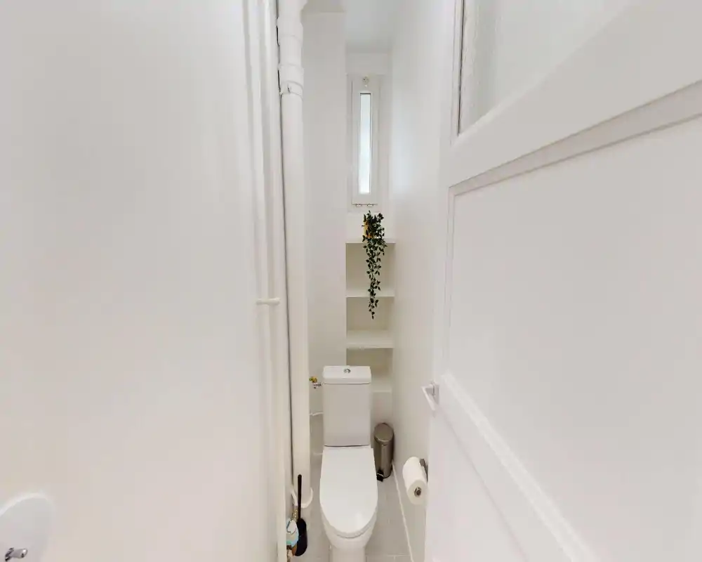 Compact, bright bathroom with a modern toilet, built-in shelving and a small high window that brings natural light.