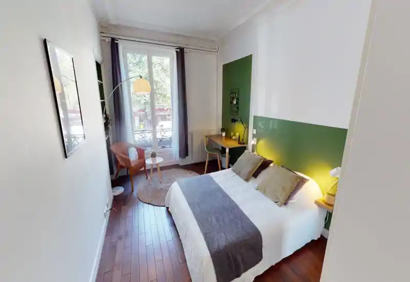 Chambre lumineuse et élégante avec lit double, textiles confortables, lampes de chevet et petit bureau près de la fenêtre. La grande fenêtre apporte une belle lumière naturelle et une ambiance moderne apaisante.