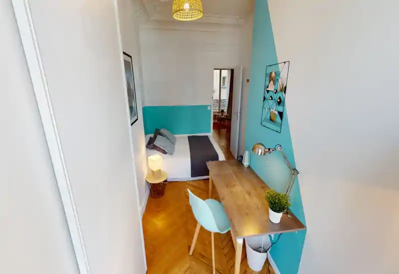 Camera da letto luminosa e di design con letto matrimoniale, lampada da comodino e scrivania in legno. Parete turchese e pavimento in parquet creano un'atmosfera moderna e accogliente.