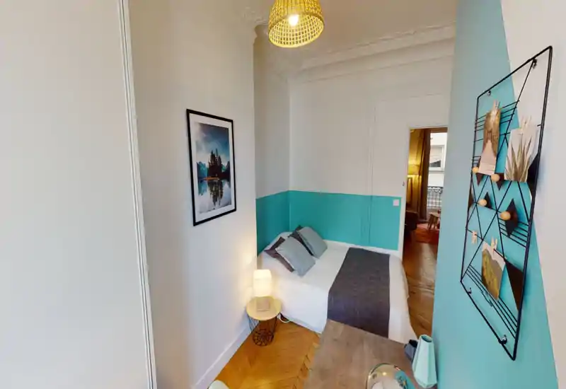 Camera da letto luminosa e di stile con un comodo letto matrimoniale, cuscini decorativi e lampada da comodino. La parete turchese e il pavimento in legno creano un’atmosfera fresca e accogliente, perfetta per soggiorni brevi.