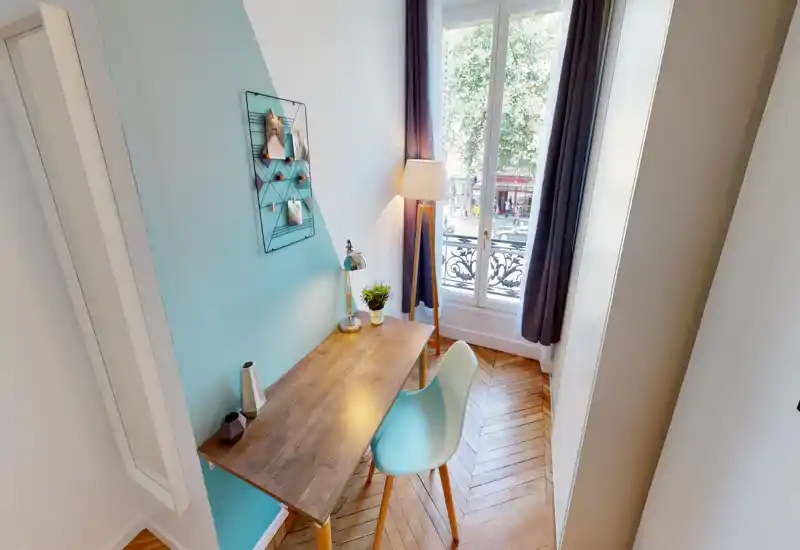 Angolo luminoso e ricercato con scrivania in legno, sedia moderna e lampada da terra vicino a una grande finestra che lascia entrare luce naturale — perfetto come spazio di lavoro accogliente nel soggiorno.