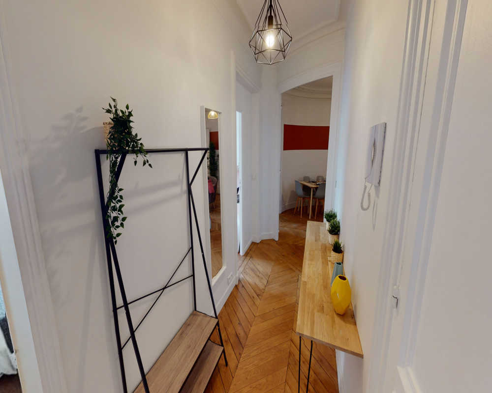Entrée lumineuse et moderne avec parquet en chevrons, une console fine avec vases et plantes et un porte-manteau—première impression accueillante.