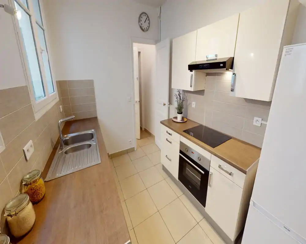 Cuisine moderne en ligne avec plans de travail en bois, four intégré et plaque à induction, évier en inox et réfrigérateur — lumineuse et bien organisée pour cuisiner.