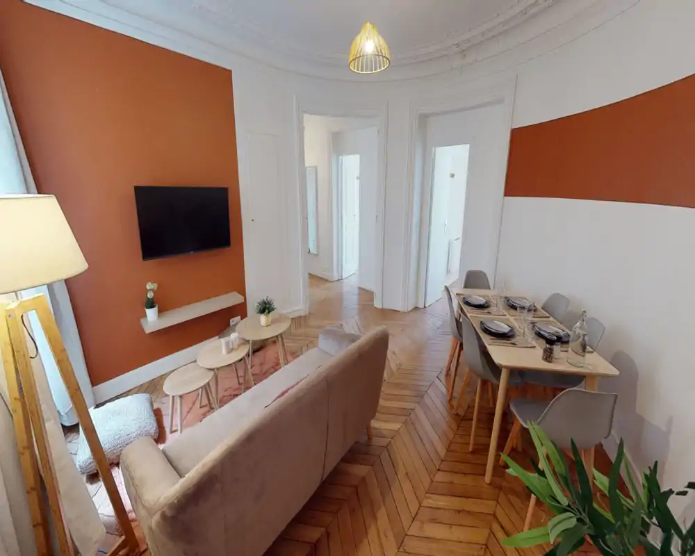 Séjour lumineux et élégant avec canapé douillet, télévision murale, tables basses gigognes et table à manger pour six. Mur d'accent terracotta et parquet en chevrons apportent caractère et convivialité.