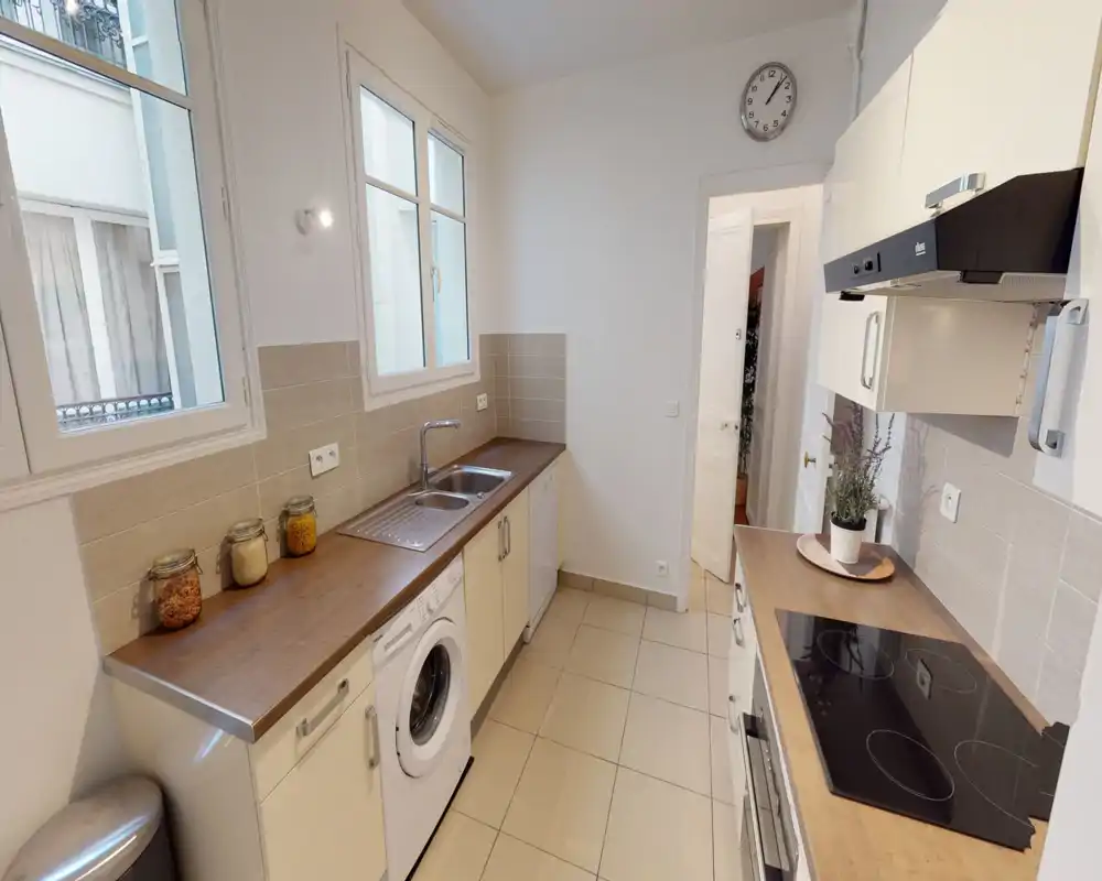 Cuisine en enfilade lumineuse et soignée avec plans de travail en bois, plaque à induction, évier et appareils intégrés — idéale pour un appartement urbain compact.