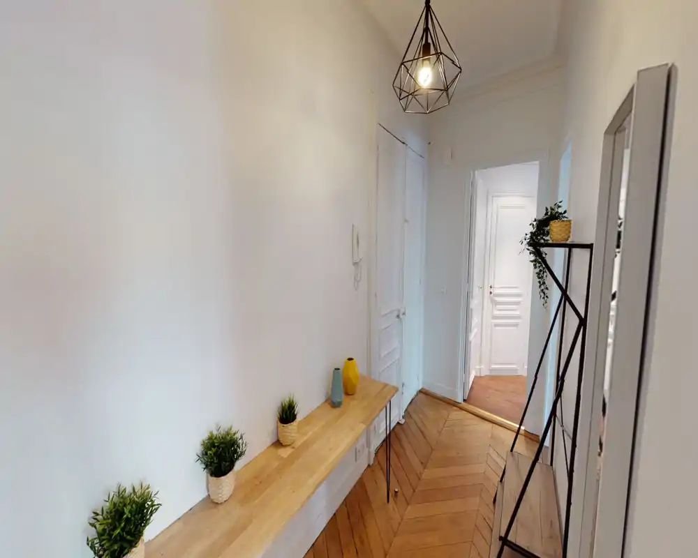 Entrée lumineuse et soignée avec parquet chevron, banc étroit agrémenté de plantes et vases décoratifs, et suspension moderne au plafond.