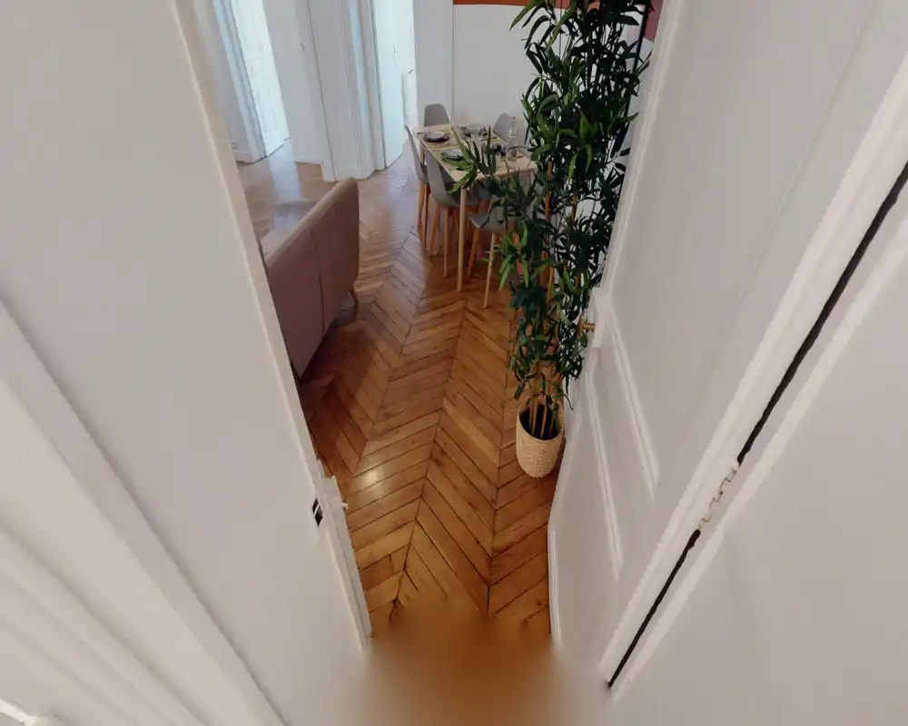 Espace salon/salle à manger contemporain avec parquet en chevrons, un petit canapé, une table dressée et une grande plante d’intérieur — lumineux, confortable et élégant.