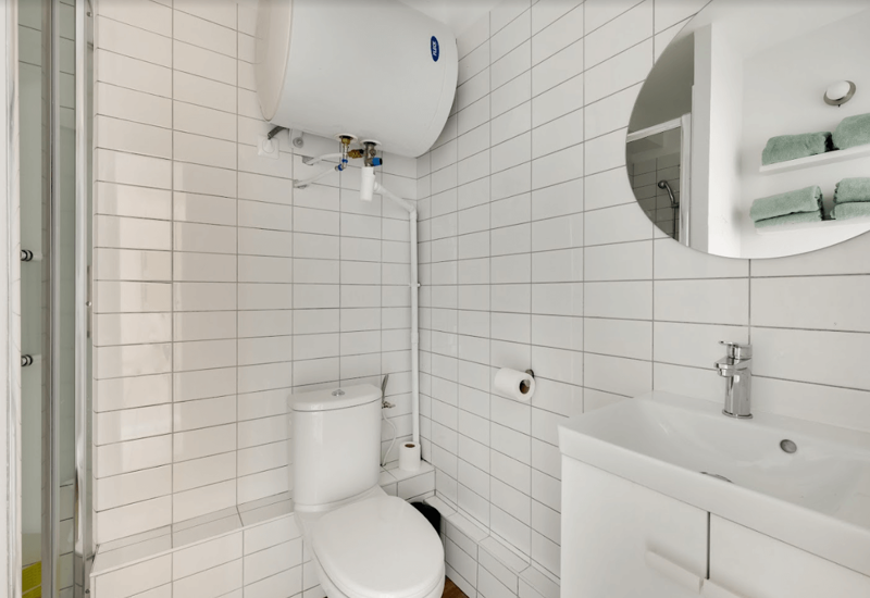 Compact modern bathroom with white subway tiles, toilet, sink with vanity and a round mirror. Clean, bright and efficiently arranged for small spaces.