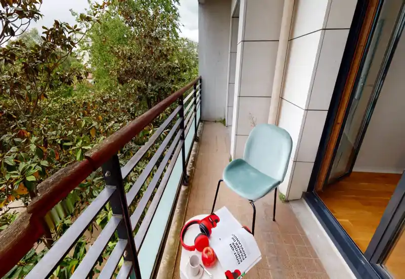 Balcon ensoleillé avec une rambarde métallique, une chaise moderne et une petite table avec un casque, une tasse et un livre — idéal pour un café matinal en extérieur.