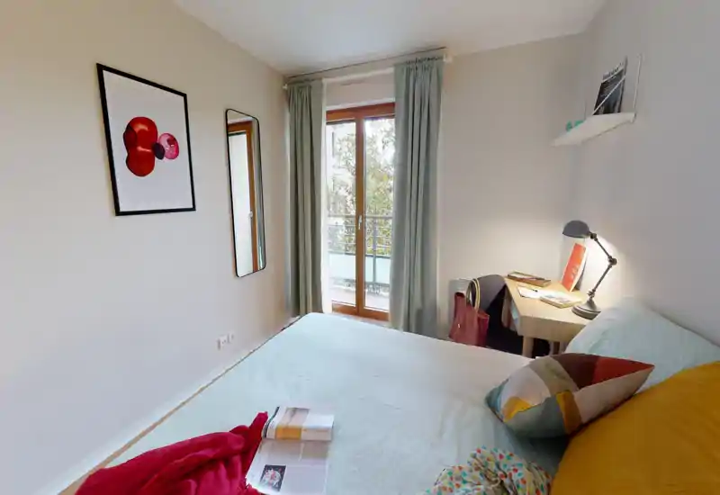 Chambre lumineuse et bien mise en scène avec un grand lit confortable, coussins décoratifs et un petit bureau près de la fenêtre laissant entrer la lumière naturelle.