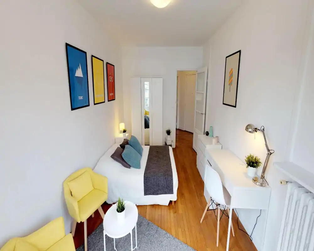 Chambre lumineuse et moderne avec lit double, plaid et coussins confortables, armoire blanche avec miroir et un bureau soigné — mise en scène idéale pour une annonce.