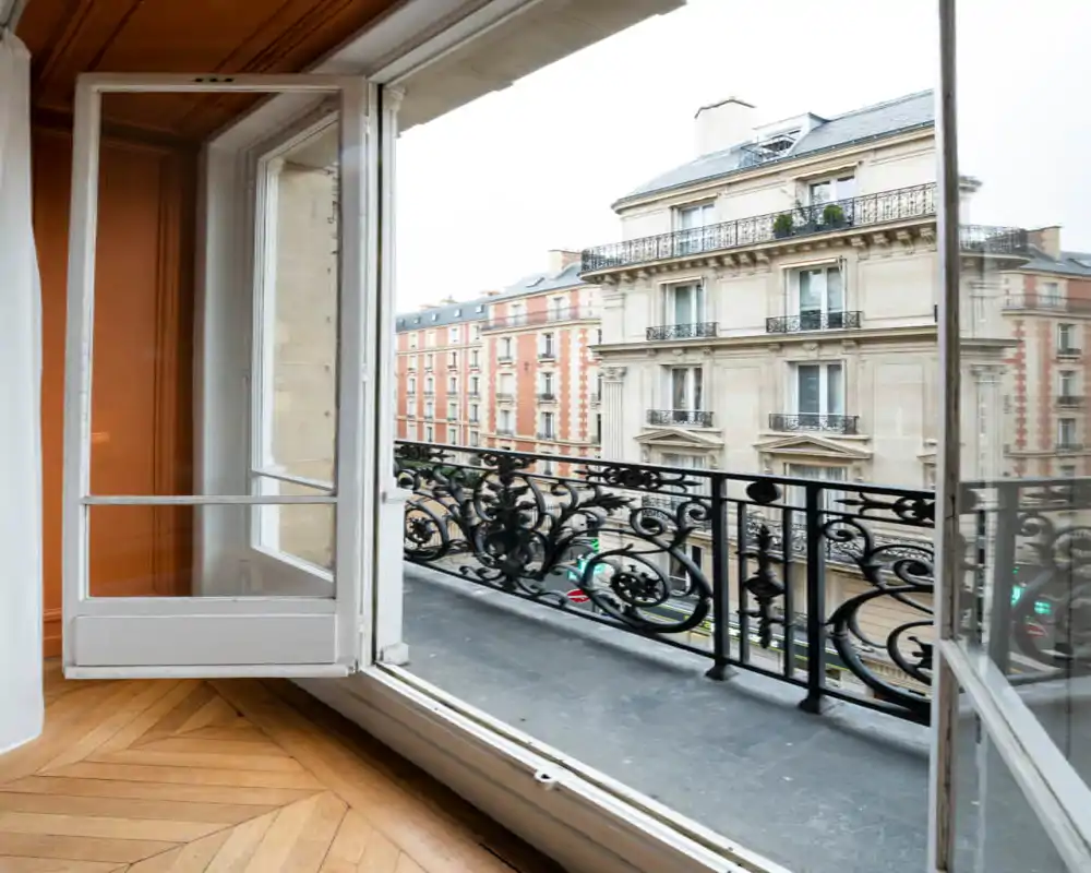 Balcón de estilo francés visto desde el interior, con barandilla de hierro forjado decorativa y vistas a elegantes fachadas parisinas.