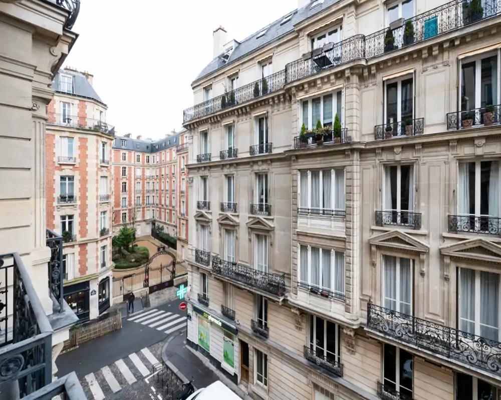 City view from a balcony overlooking classic Parisian buildings, street, and a small courtyard; neutral daylight and architectural details.