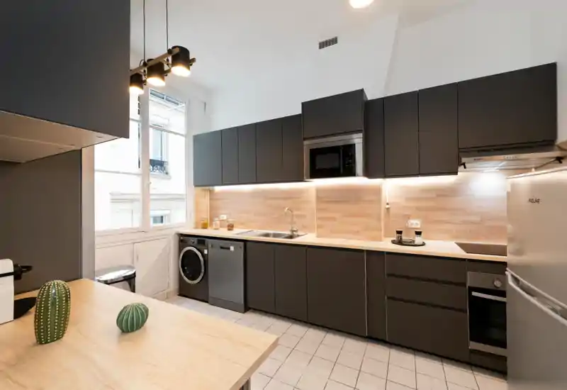 Modern, fully equipped kitchen with dark matte cabinets, wooden countertops and backsplash, integrated appliances and a bright window — ideal for stylish apartment listings.