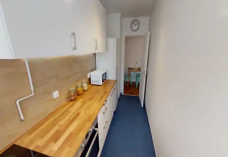 Narrow galley kitchen with warm wooden countertops, white cabinets and practical appliances; bright, clean and efficiently arranged for small-space living.
