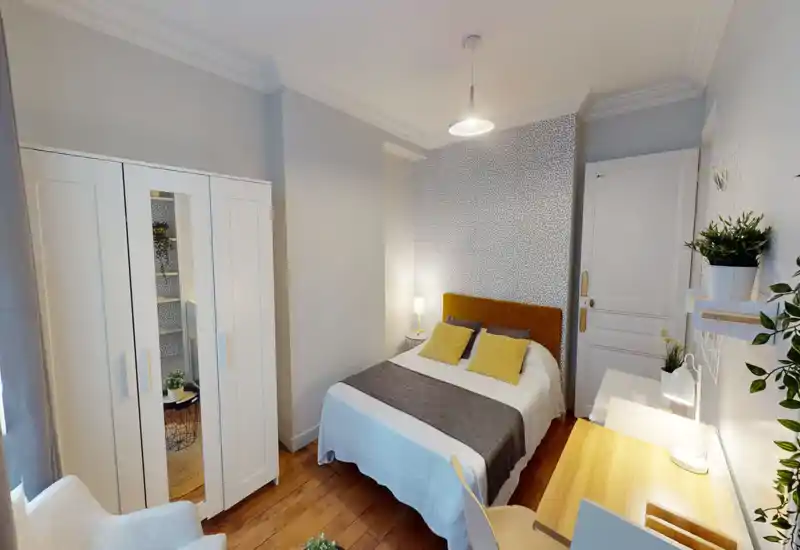 Camera da letto luminosa e di design con letto matrimoniale comodo, parete decorativa a motivo e un pratico angolo scrivania. Pavimento in legno e cuscini coordinati donano un’atmosfera calda e accogliente.