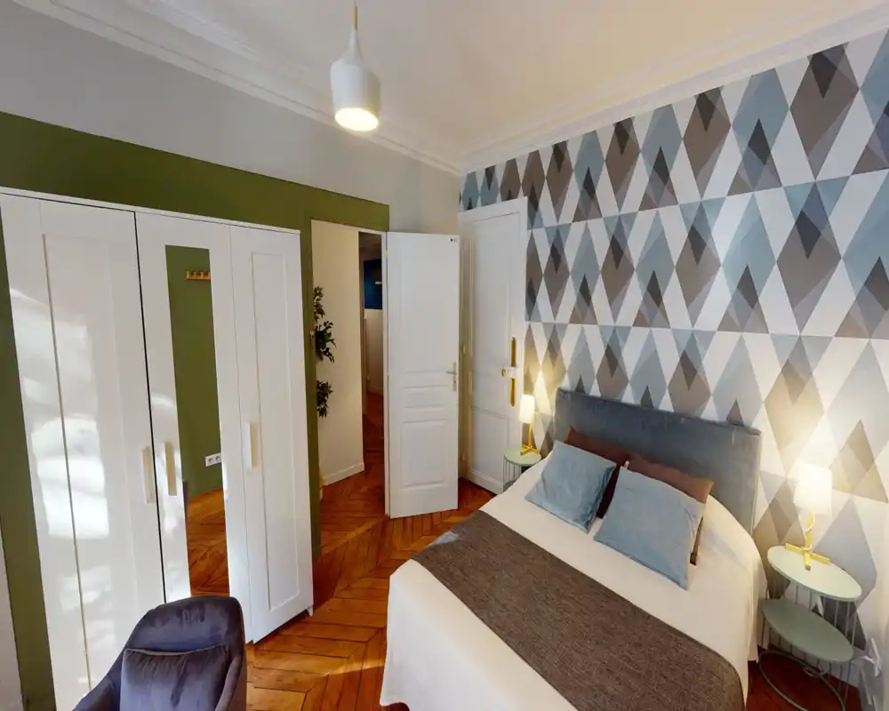 Camera da letto luminosa e di stile con letto ampio, parete decorativa geometrica, comodini con lampade e pavimento in parquet caldo — uno spazio accogliente e ben illuminato, perfetto per foto dell'annuncio.