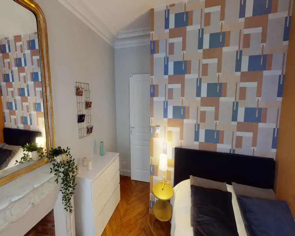 Chambre lumineuse et élégante avec un mur à motifs, grand lit confortable et lampe de chevet — une ambiance chaleureuse et bien décorée, idéale pour les annonces.