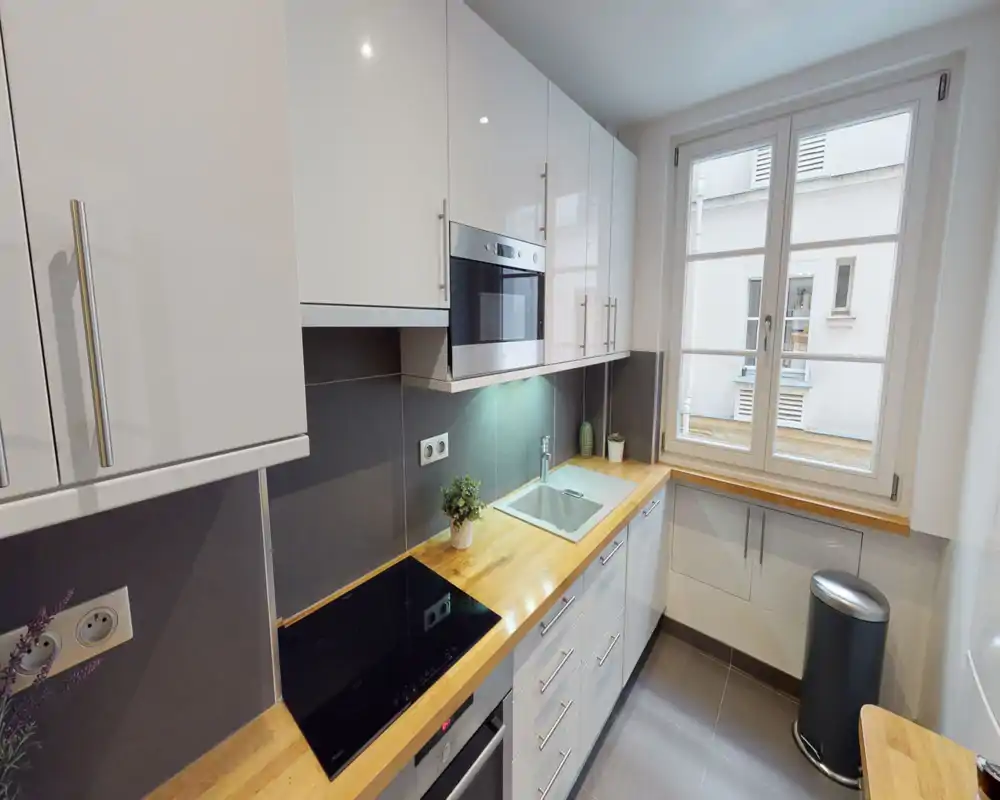 Modern, compact kitchen with white cabinetry, wood countertops, induction hob, built-in oven and a large window providing natural light.