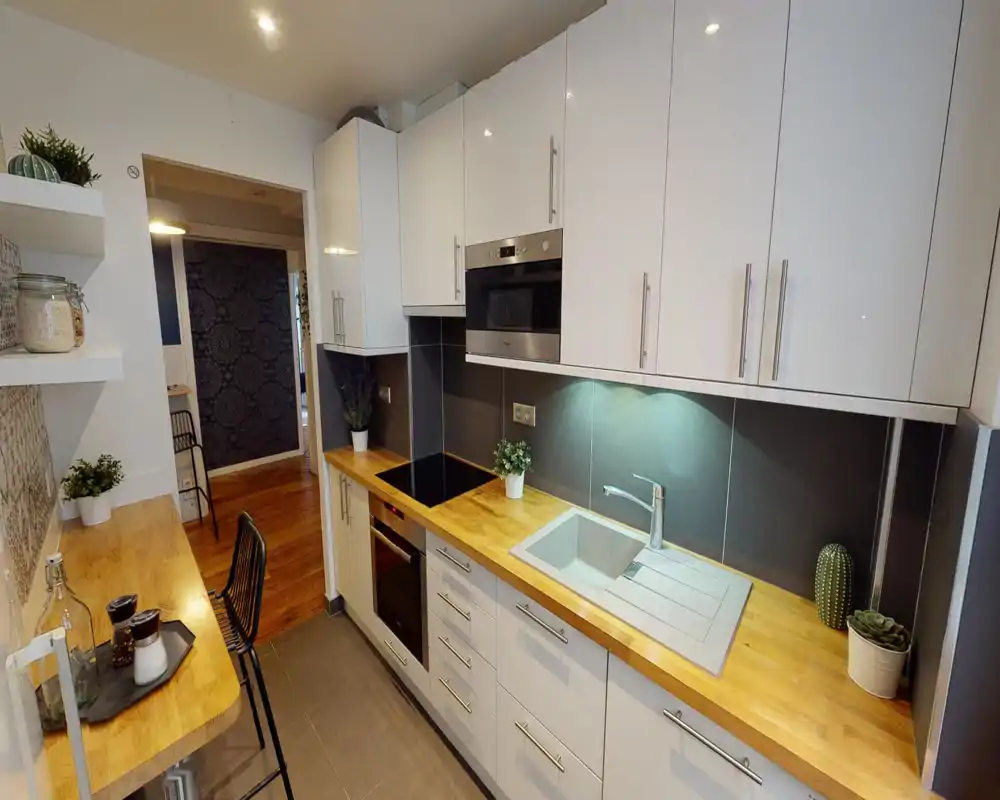Modern fitted kitchen with white cabinets, wooden countertops, integrated oven and induction hob. Bright, well-organized space with small plants and decorative jars for a welcoming touch.