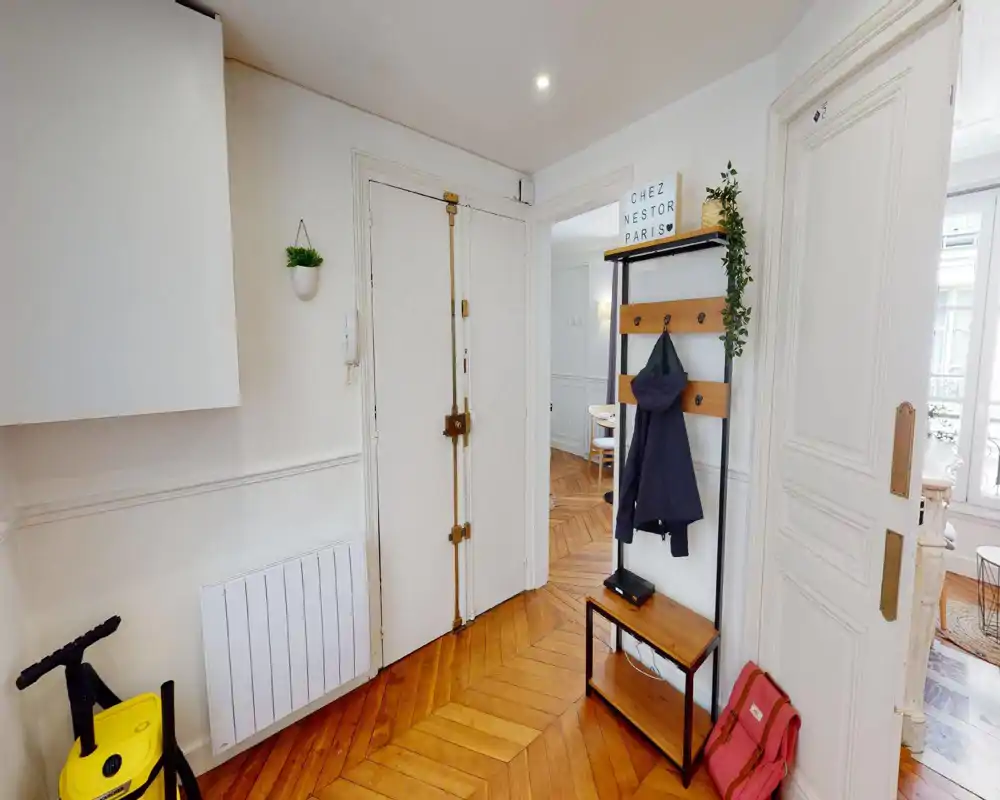Bright, tidy entrance with a wooden herringbone floor, wall-mounted coat rack and storage bench — ideal first impression for guests.