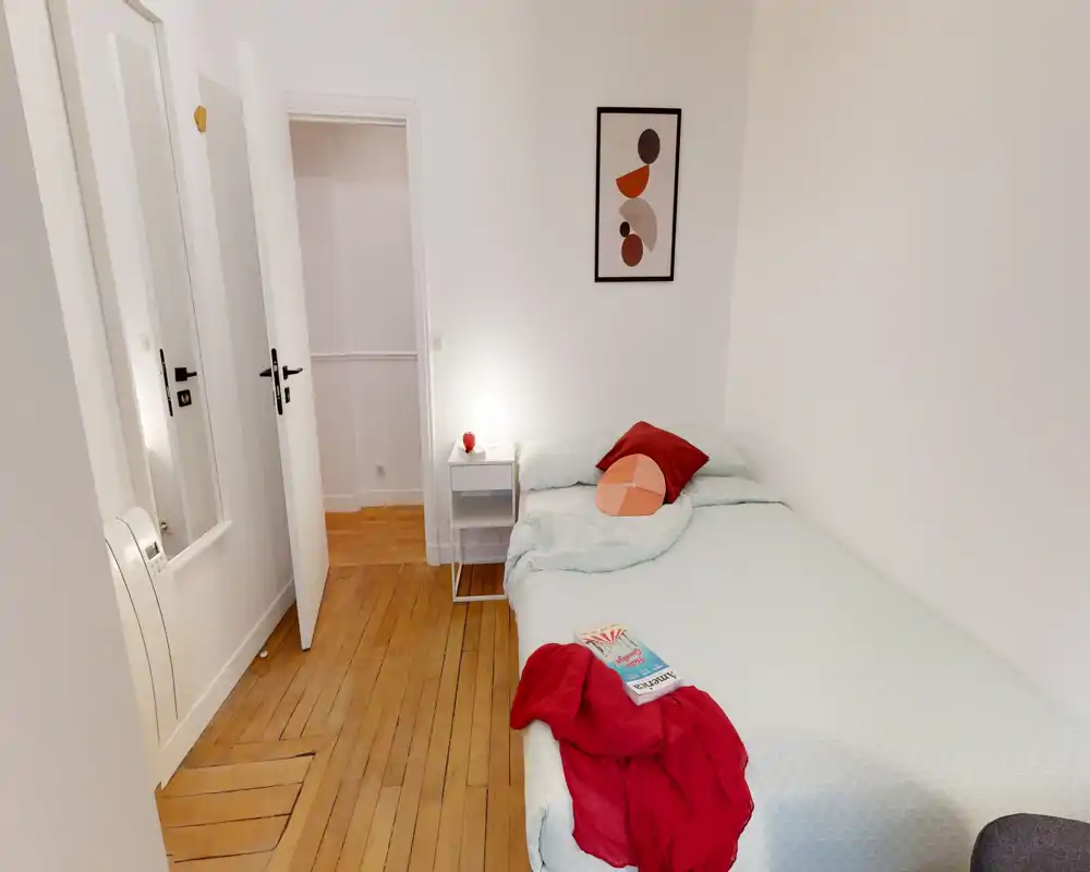 Small, neatly styled single bedroom with a comfortable bed, soft bedding, bedside table and warm wooden floor — bright and welcoming for a solo guest.