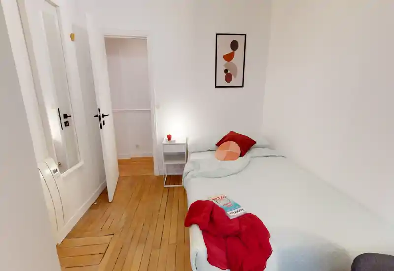 Small, neatly styled single bedroom with a comfortable bed, soft bedding, bedside table and warm wooden floor — bright and welcoming for a solo guest.