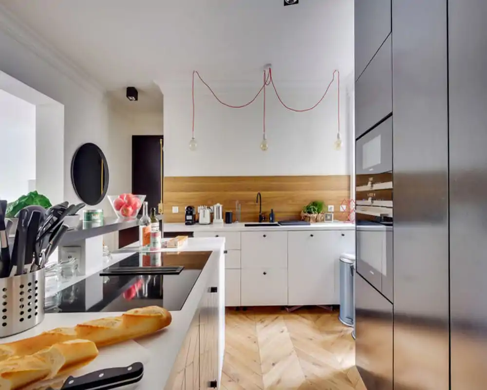 Bright, modern kitchen with a white island, built-in appliances and warm wooden backsplash — stylish, well-lit space ideal for cooking and entertaining.