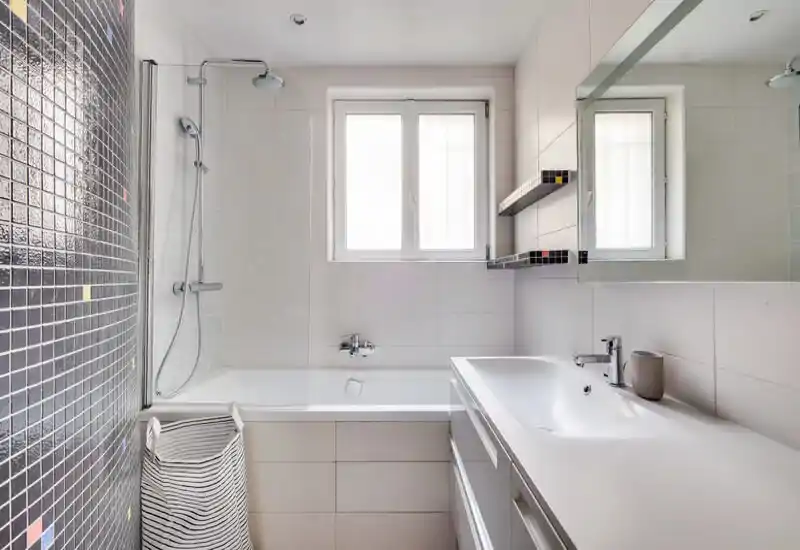Bright, modern bathroom with a bathtub and overhead shower, white tiles and a clean sink area with mirror and storage.