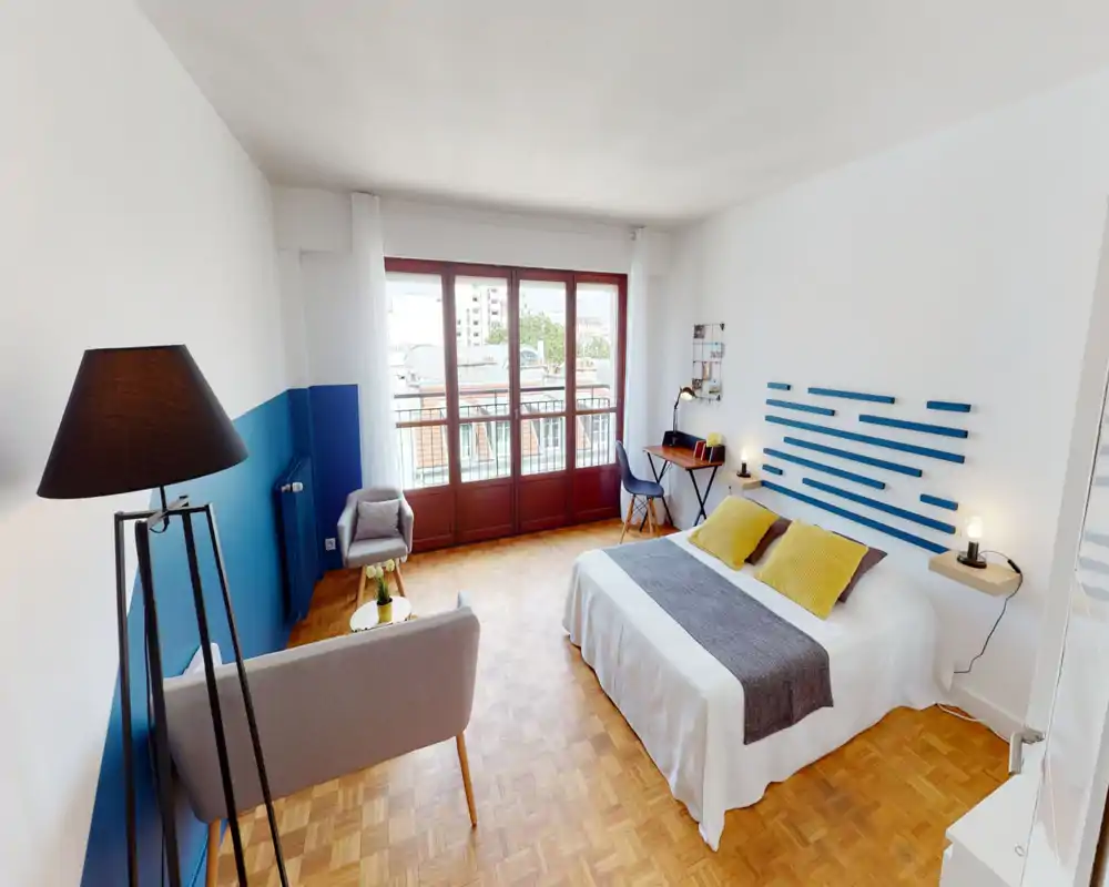 Bright, well-styled bedroom with a double bed, yellow accent pillows, bedside lamps and large windows providing ample natural light.