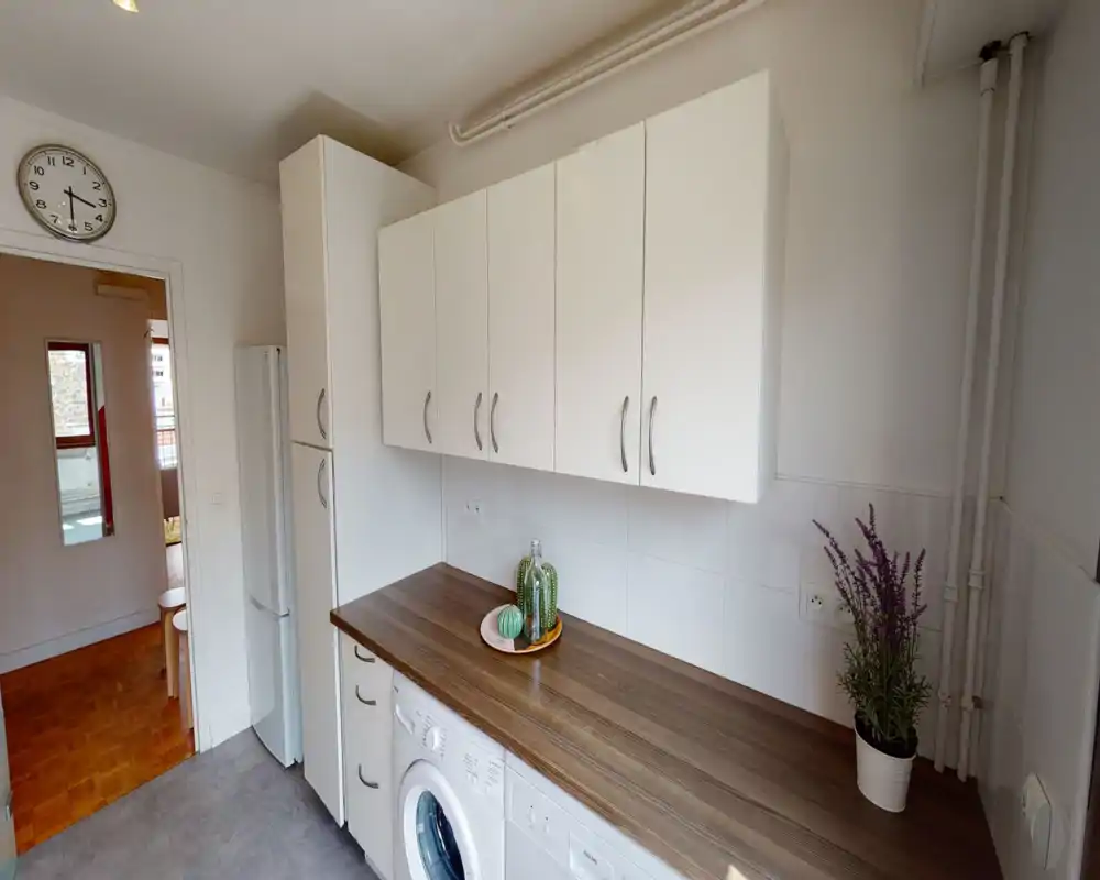 Compact, well-organised kitchen with white wall cabinets, a wooden countertop and integrated appliances. Small decorative plants and clean tile backsplash create a neat, welcoming space ideal for apartment listings.
