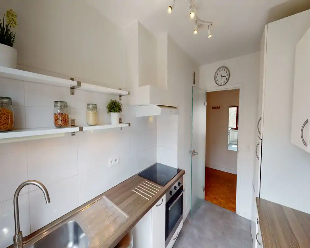 Compact, modern kitchen with a wooden countertop, induction hob and built-in oven; open shelving with jars and a small plant creates a neat, practical space.