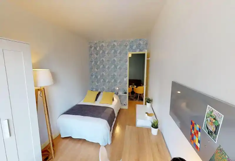 Camera da letto luminosa e ben arredata con letto matrimoniale, parete decorativa a motivi e pavimento in legno chiaro. Spazio accogliente, ben illuminato e valorizzato da cuscini coordinati e piante.