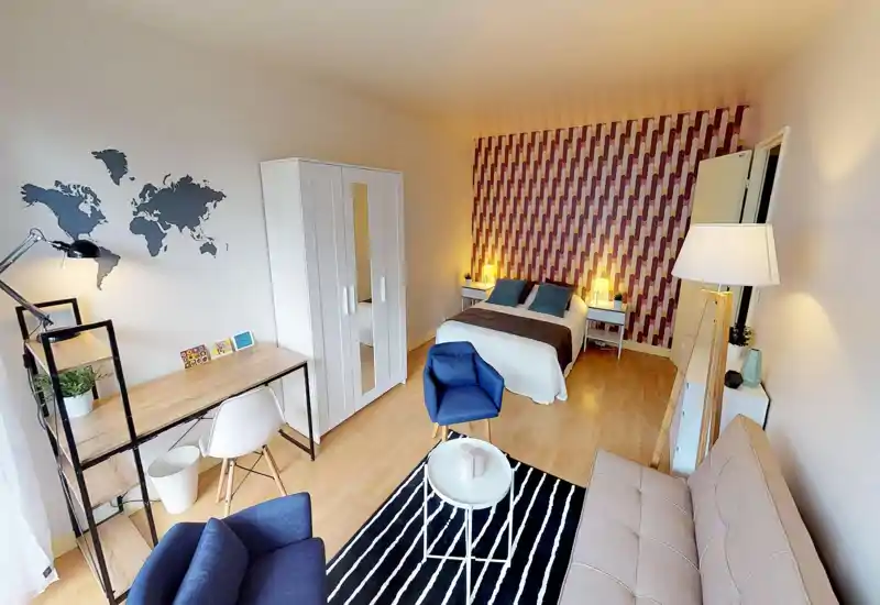 Spacious, well-decorated studio bedroom with a double bed, patterned accent wall, bedside lamps and a small seating area. Includes a desk, wardrobe and cozy textiles — bright and ready for guests.