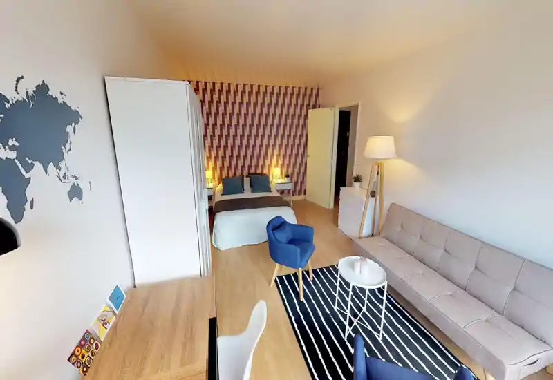 Bright, well-styled studio bedroom with a double bed against patterned wallpaper, bedside lamps, wardrobe and a seating area with sofa and armchairs — ideal for a comfortable short or long stay.