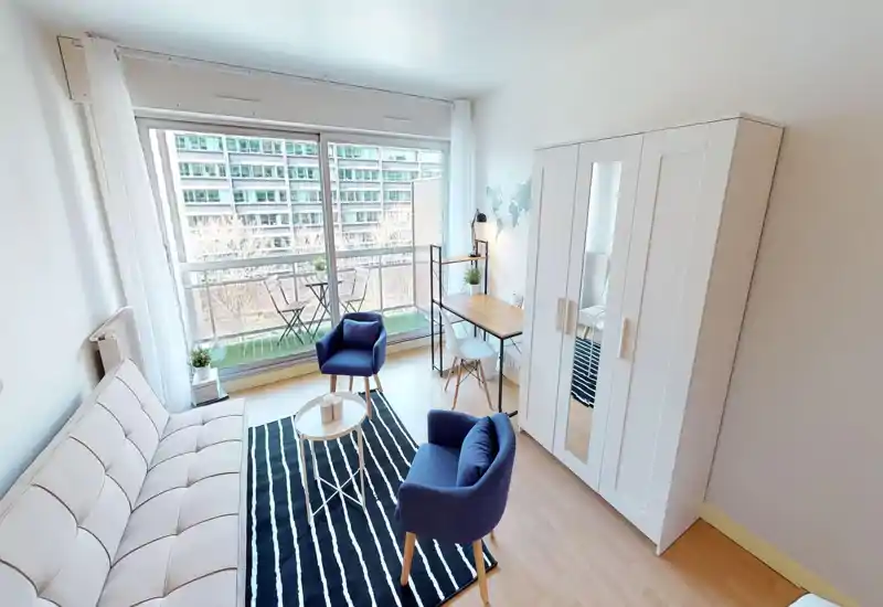 Bright, modern living area with a comfortable sofa, two armchairs, a coffee table and a work desk next to large floor-to-ceiling windows leading to a small balcony.