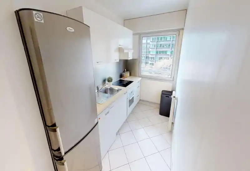 Compact modern kitchen with white cabinets, built-in oven and hob, stainless fridge and a bright window that brings natural light.