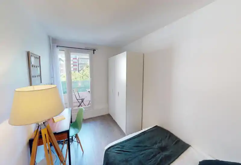 Bright bedroom with a double bed and bedside lamp; bedding and simple decor create a welcoming atmosphere despite image artifacts.