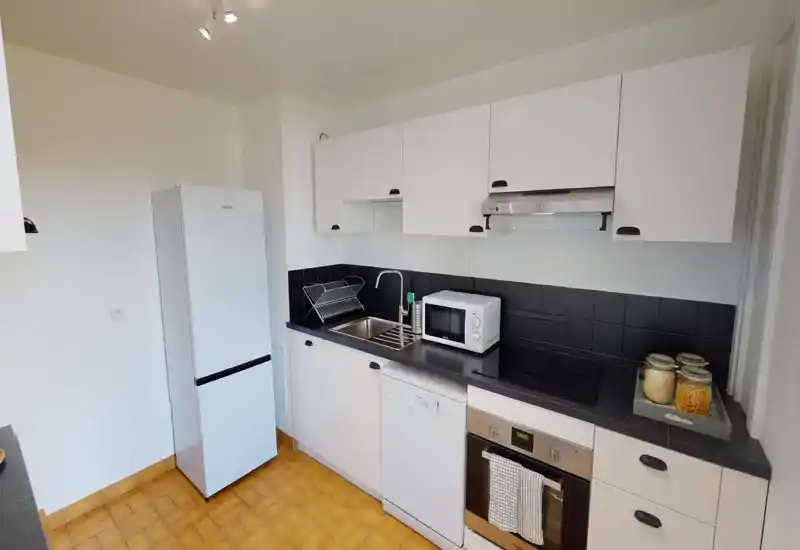 Bright, compact kitchen with white cabinets, black countertop and tiled backsplash. Includes fridge, oven, dishwasher and a microwave — ideal for functional everyday cooking.
