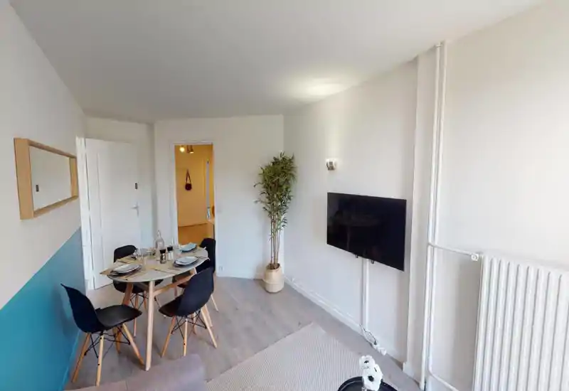 Bright, modern living/dining area with a small round dining table set for four, wall-mounted TV and decorative plant—an inviting open-plan space ideal for relaxed meals and TV evenings.