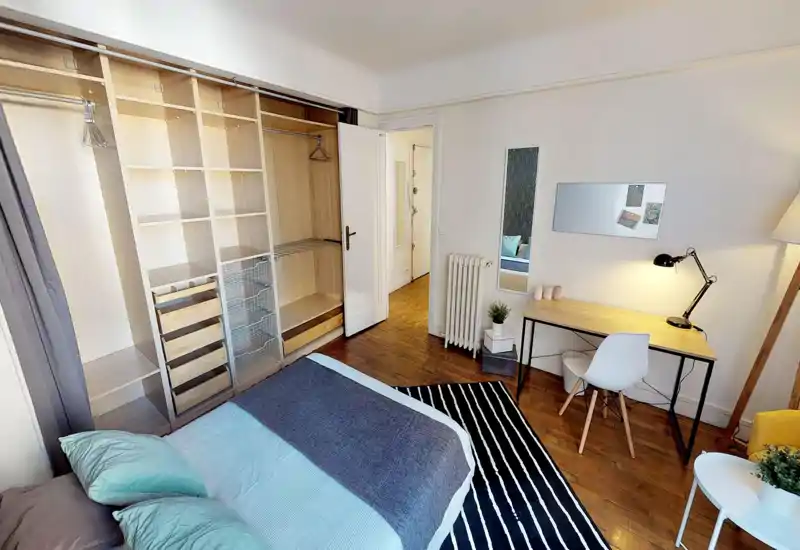 Camera da letto luminosa e ben arredata con un ampio letto, armadio a vista integrato e una postazione di lavoro. Pavimenti in legno e tessili morbidi creano un'atmosfera accogliente e moderna.