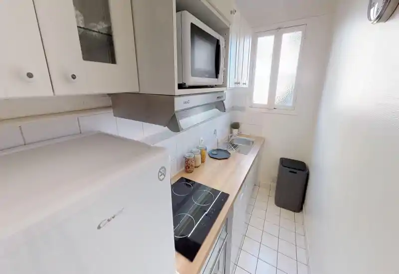 Cucina a corridoio compatta e luminosa con piano di lavoro in legno, piano a induzione, microonde e lavello; piastrelle bianche e contenitori ordinati creano uno spazio pulito e funzionale.