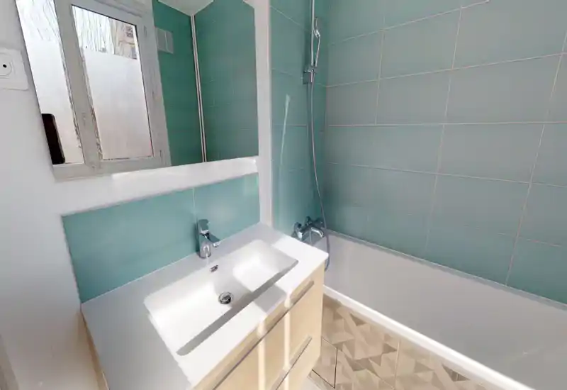 Salle de bains moderne et lumineuse avec vasque blanche, baignoire et carreaux turquoise. Lignes épurées et lumière naturelle pour une ambiance fraîche et fonctionnelle.